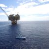 A boat in the ocean near an oil rig.